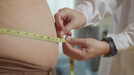 close up side view of male doctor's hands using tape measuring fat male patient's waist