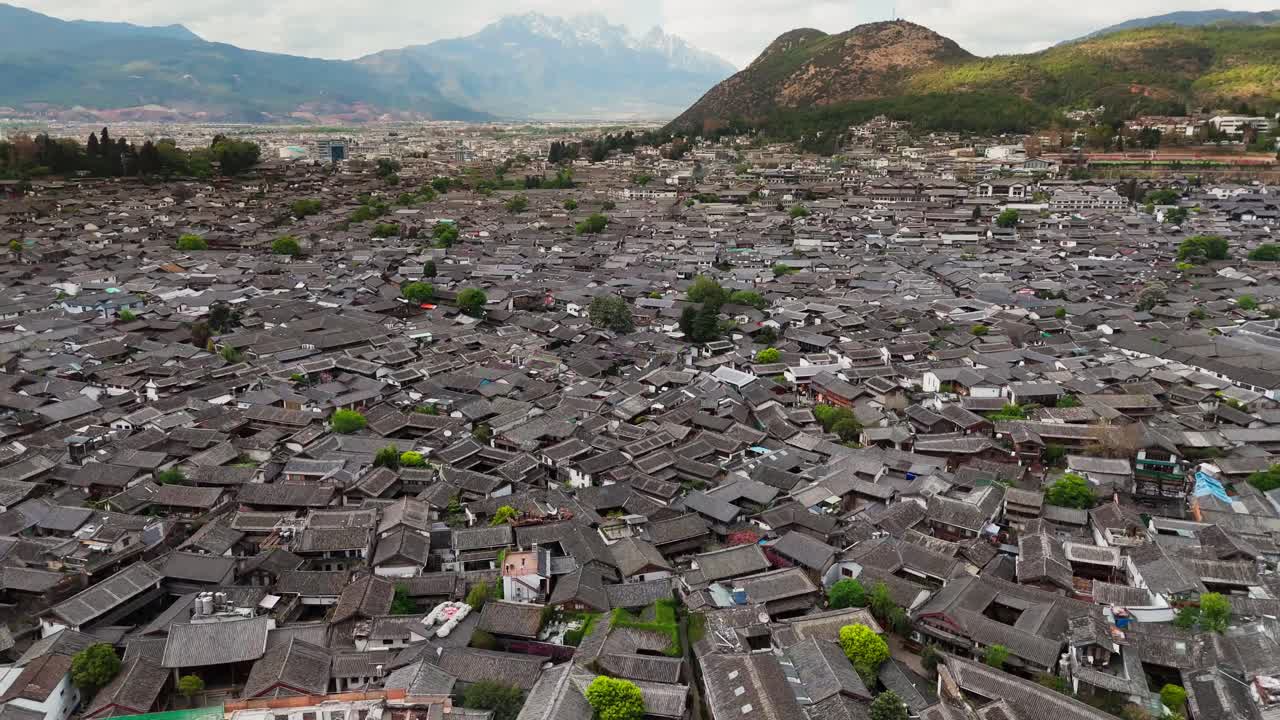 Aerial view of Dayan, the Old Town of Lijiang, in Yunnan, China, traditional Chinese architecture and snow mountains at distance drone above cityscape