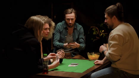 grupo de amigos jugando al póquer sentados en sillas en una mesa en casa