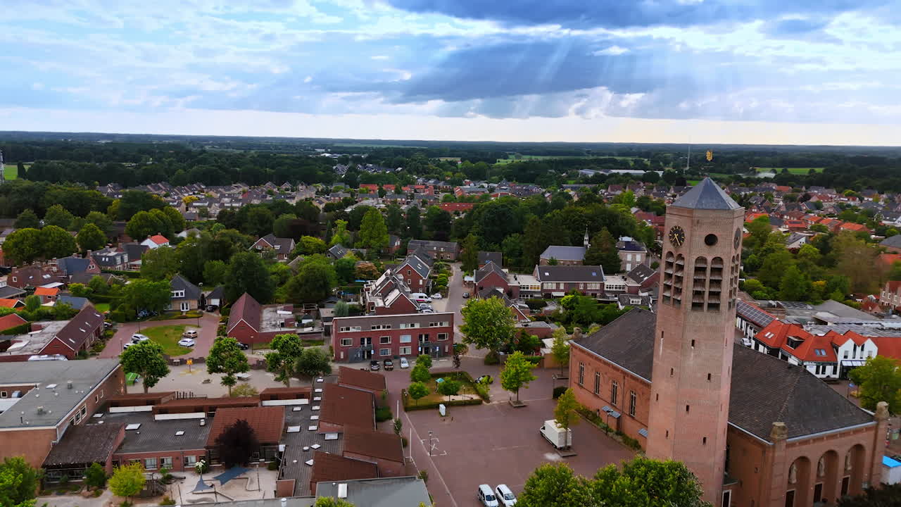 Green panorama of modern Vierlingsbeek, Netherlands. Footage near the brick clock tower of Saint Lawrence Church. Sun beams go through the clouds in the sky