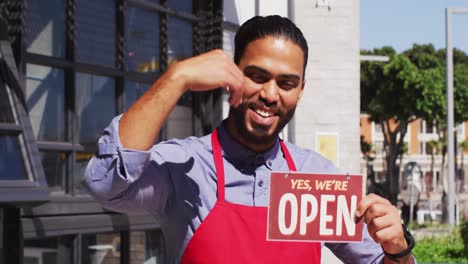 happy mixed race male cafe worker showing were open signage and smiling