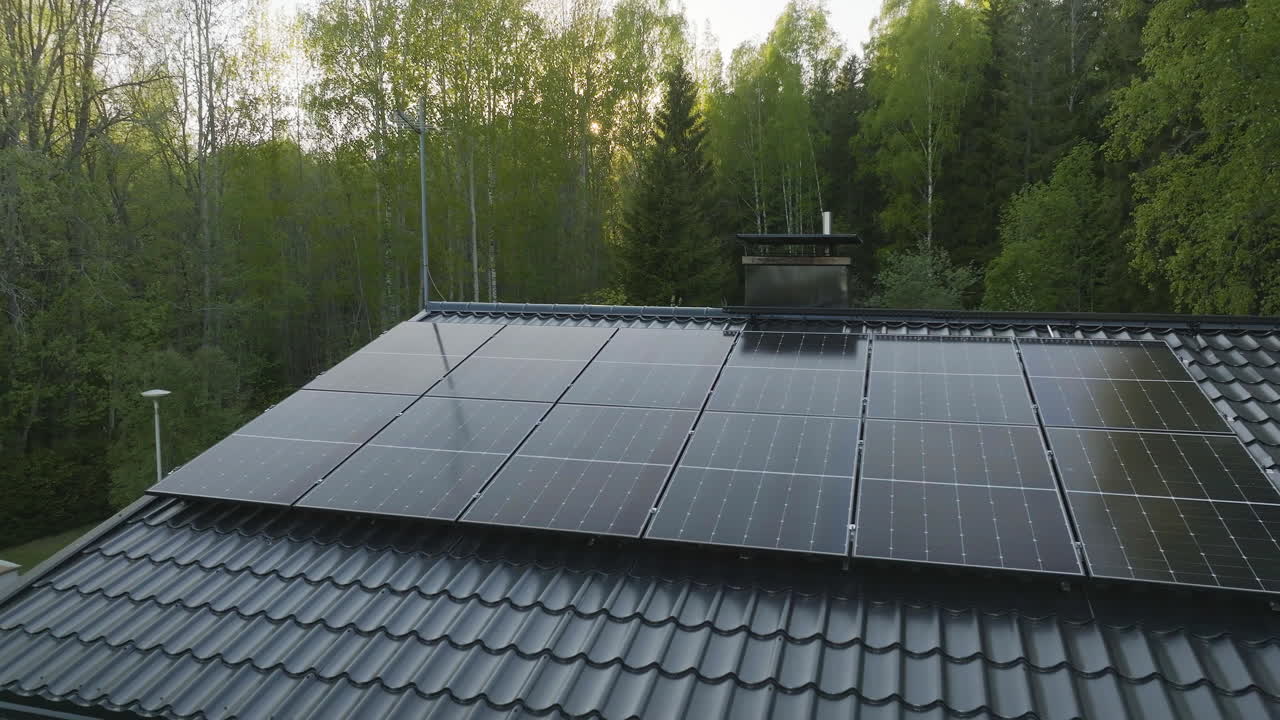 Drone shot of a house roof with sunlight collectors in middle of spring forest