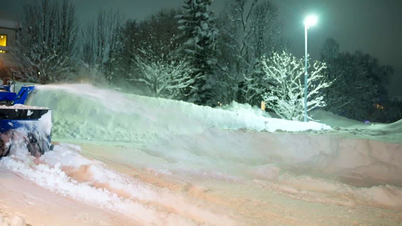 An adult man using snowblower gasoline machine to clear deep snow from front of residential house after heavy snowfall at night