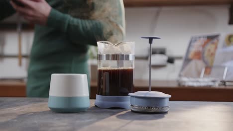 Midsection-of-caucasian-man-making-coffee-and-using-smartphone-in-kitchen,-slow-motion