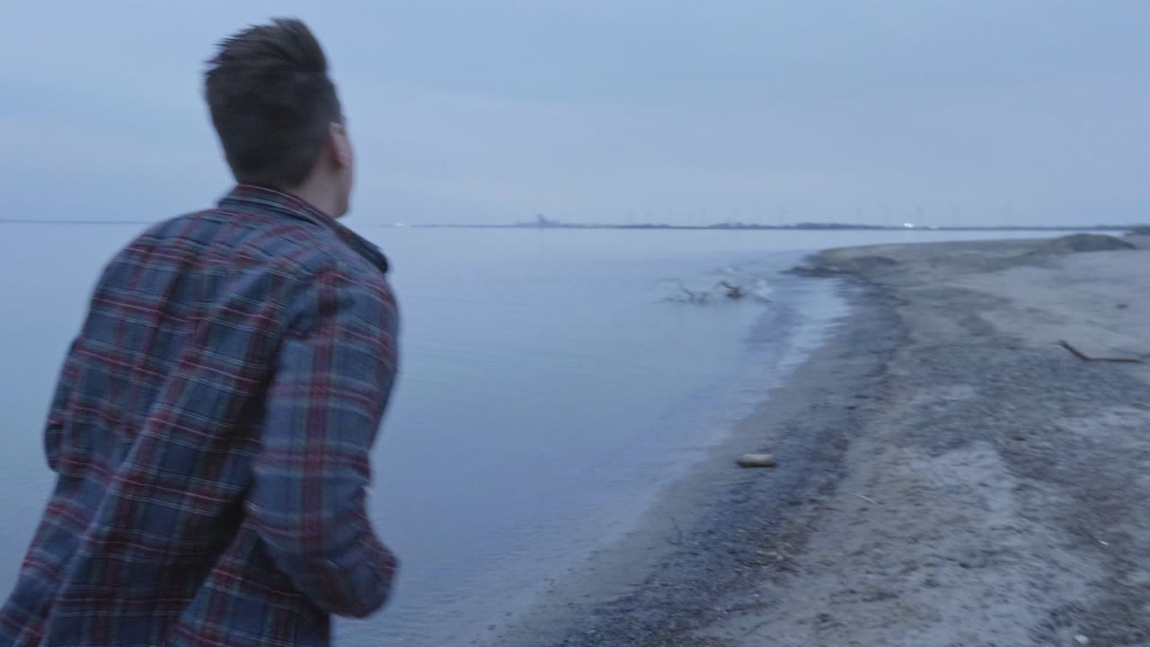 느린 동작으로 호수 옆의 차가운 해변에서 달리는 백인 남자