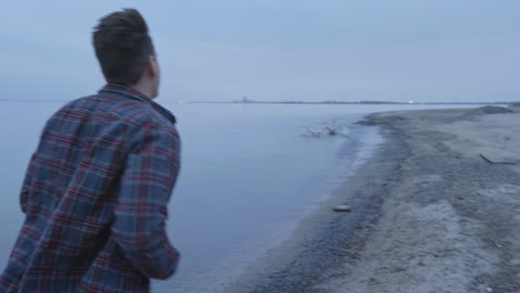 hombre caucásico corriendo en una playa fría junto a un lago en cámara lenta