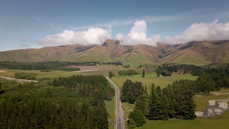 aerial - state highway 8 leading through farm land and high mountains in new zealand