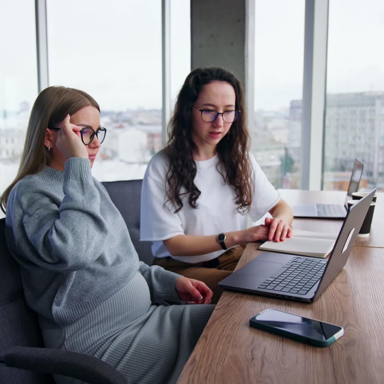 Female colleagues sit in the office working on laptop. Workmates discussing the project