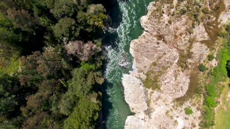 slow overhead drone tracking a turquoise blue river gorge flowing through the lush green forest canopies and deep canyons of new zealand