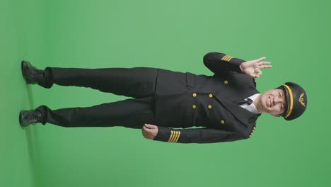 아시아 남성 조종사가 미소 짓고 녹색 스크린 배경 스튜디오에 서있는 동안 카메라에 은 몸짓을 보여주고 있습니다.