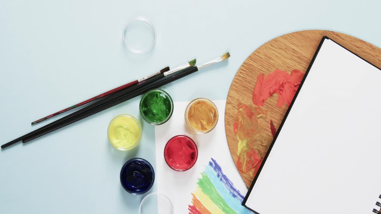 슬로우 모션으로 파란색 배경에 노트북, 브러시 및 페인트의 오버헤드 뷰