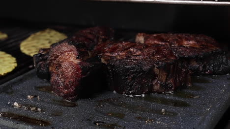 Thick-juicy-steaks-sizzle-in-outdoor-barbeque-grill-in-backyard-and-person-closes-lid,-close-up