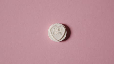 Hand-Picking-Up-Heart-Candy-With-True-Love-Message-On-Pink-Background