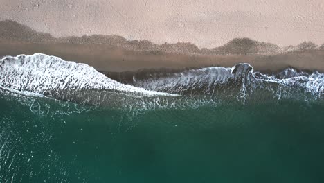 Aerial-birdseye-view-of-blue-water-waves-crashing-on-yellow-sandy-beach