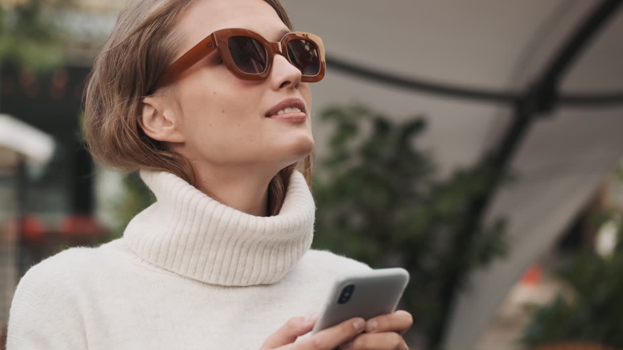 mujer caucásica con gafas de sol usando un teléfono inteligente al aire libre.