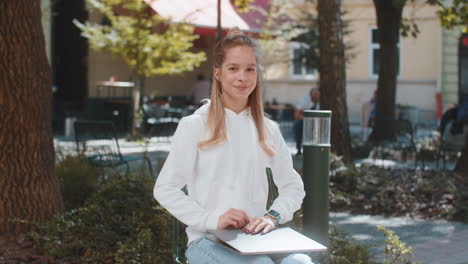 happy young woman freelancer sitting in city street closes laptop screen finishing working online
