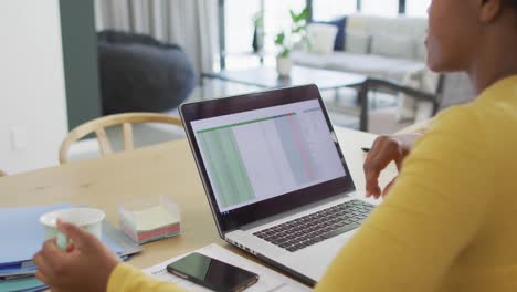happy african american woman sitting at table using laptop and drinking coffee