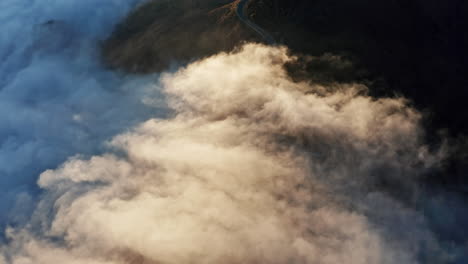 A-winding-road-shrouded-in-mist-during-sunrise,-with-dramatic-play-of-light-and-shadow,-aerial-view