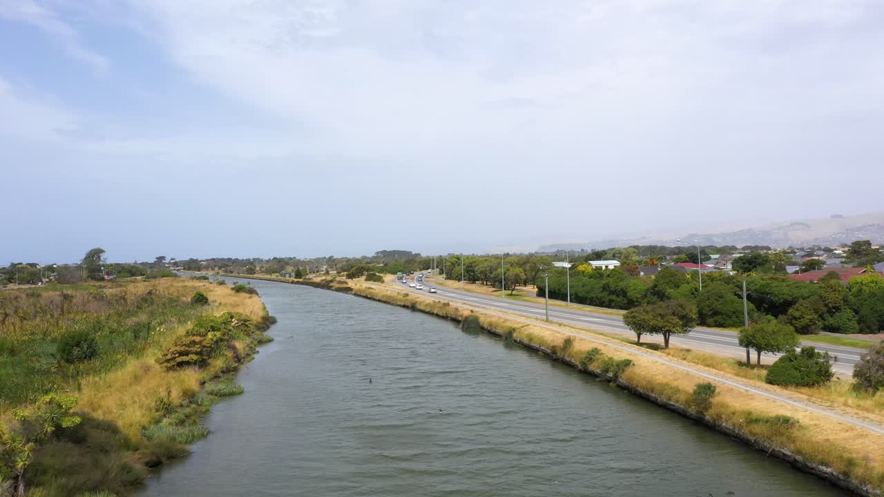 Flight over river moving towards river mouth next to road with traffic.