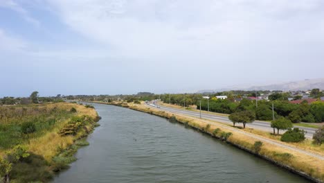 flight over river moving towards river mouth next to road with traffic.