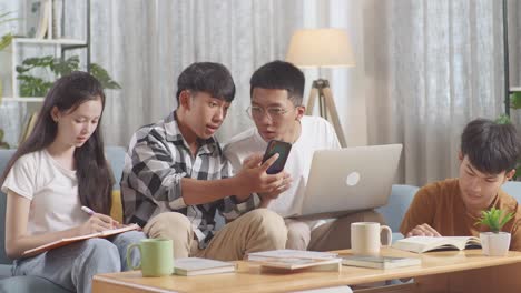 asian teen group studying at home. students with books and laptop looking at smartphone, celebrating success in project, giving high five gesture