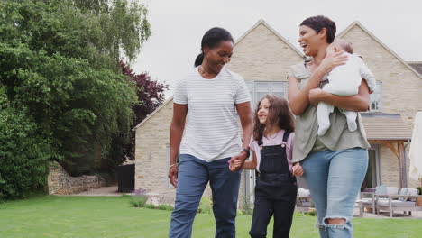 Mother-With-Daughter-And-Granddaughter-From-Multi-Generation-Family-Walking-In-Garden-At-Home