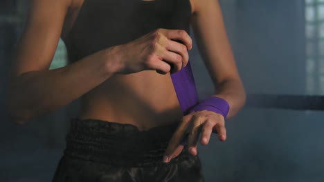 close up view of female hands being wrapped for boxing in dark room with smoke. young fit woman wrapping hands with purple boxing