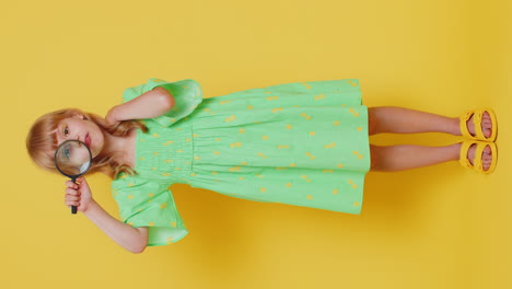 Child-kid-girl-holding-magnifying-glass,-looking-into-camera-with-big-zoomed-funny-eye,-analysing