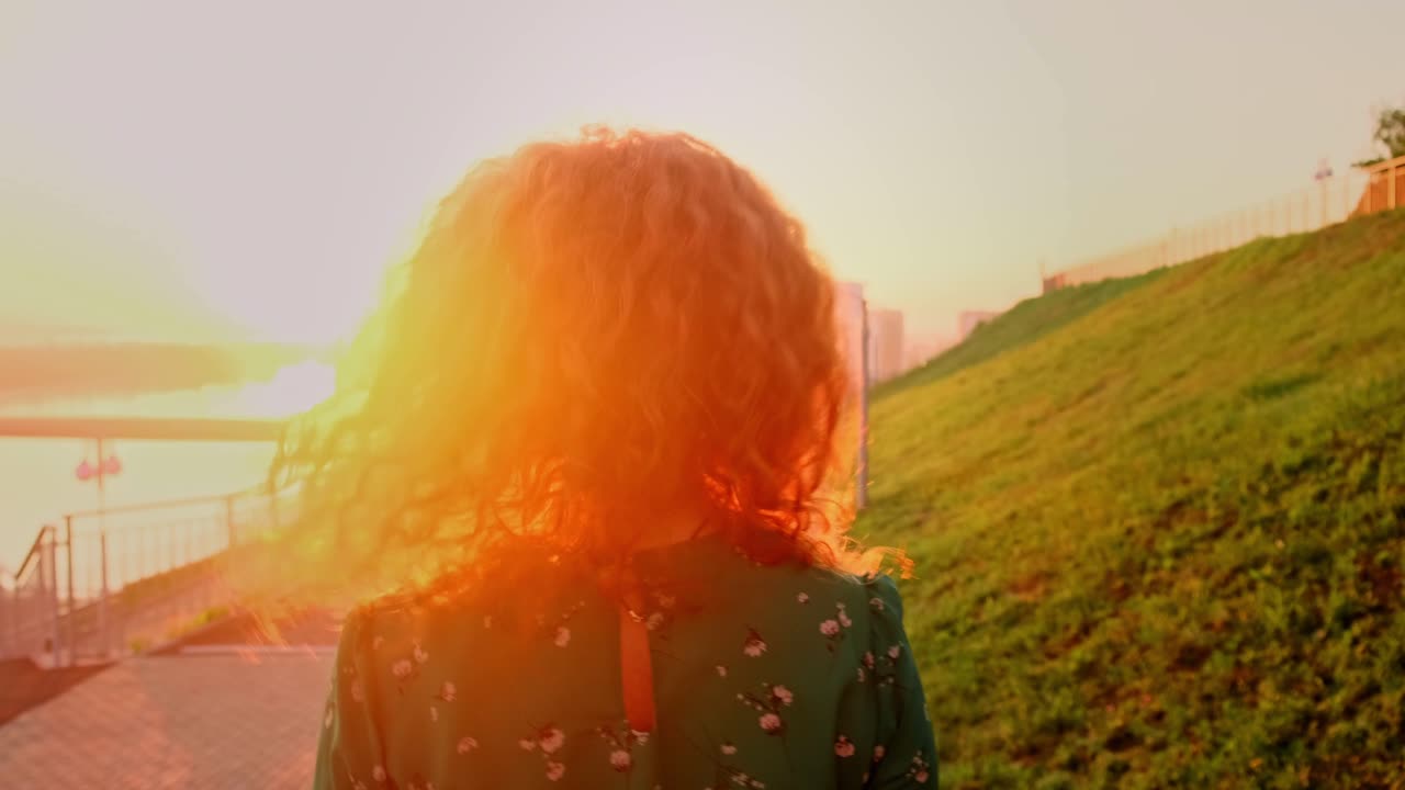 A Woman with Flowing Hair Joyfully Embraces the Evening Sunset by the Water, Taking in the Beauty of Nature as Day Transitions into Night