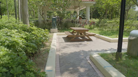 Person-POV-walking-through-empty-park-looking-at-wooden-bench-in-sun-in-hong-kong