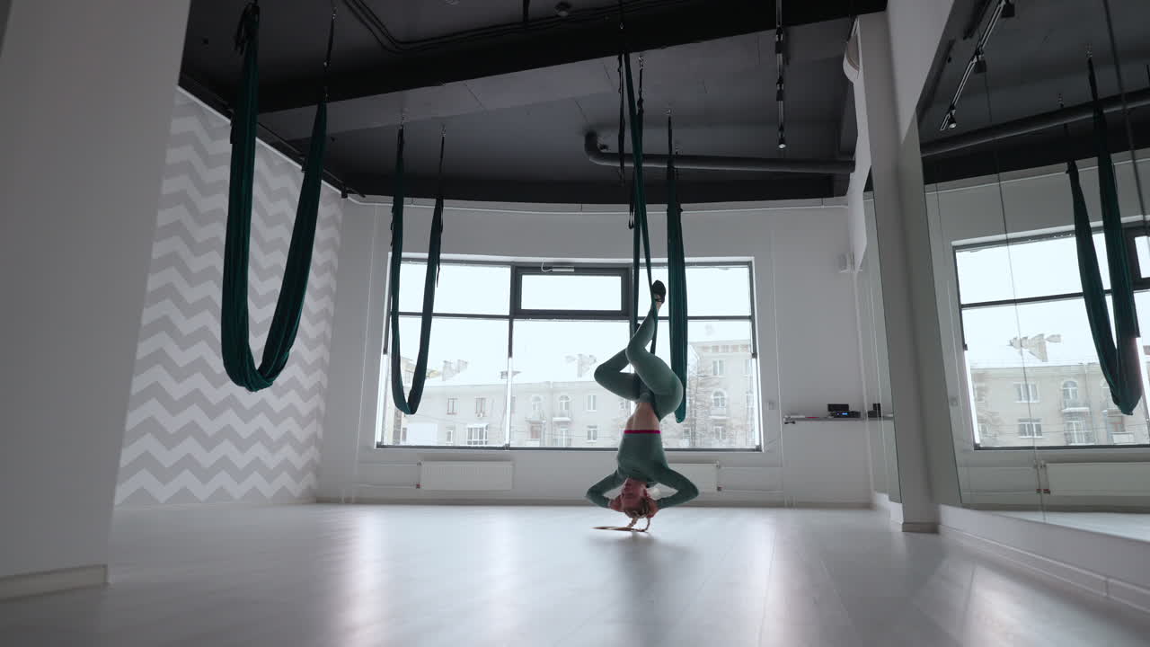 una mujer joven sonriente practicando en un columpio de estiramiento aéreo. ejercicios de yoga de vuelo aéreo practicando en una hamaca verde en un club de fitness