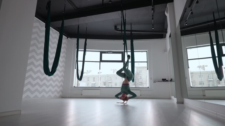 Young smiling woman practice in aero stretching swing. Aerial flying yoga exercises practice in green hammock in fitness club