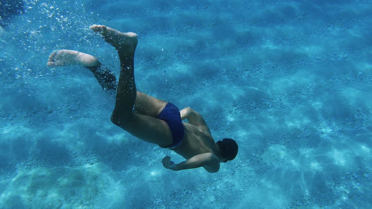 Young man free diving to the sand bottom of the sea at a beach