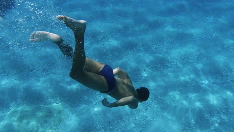 Young-man-free-diving-to-the-sand-bottom-of-the-sea-at-a-beach