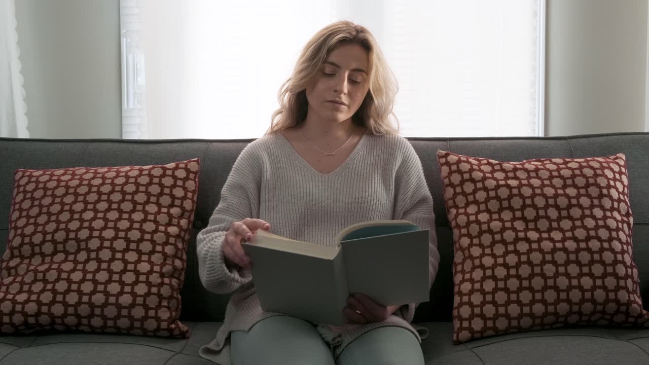 Jeune femme blonde lisant un livre chez elle