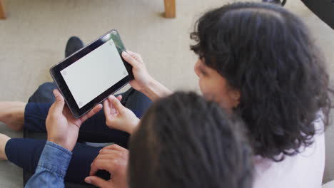 happy biracial couple sitting on couch using tablet in living room, copy space on screen