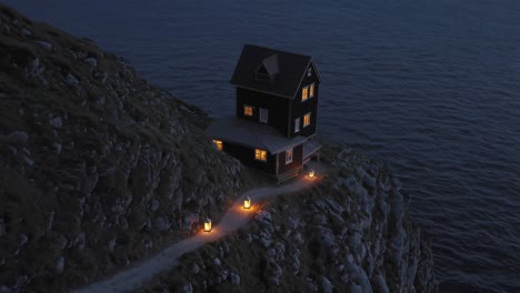 lanterns illuminate a winding path leading to a cozy cabin perched on a cliff overlooking the dark ocean at twilight, creating a tranquil and secluded atmosphere