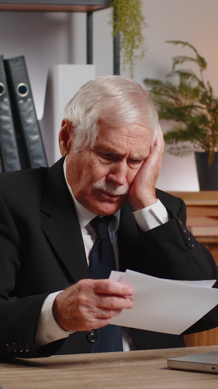 Empresario sénior abriendo un sobre leyendo malas noticias en una carta se siente molesto sentado en el escritorio de la oficina