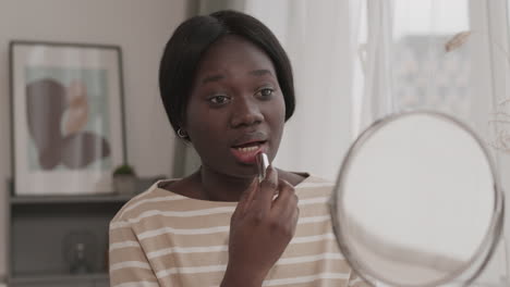 young african woman applying lipstick