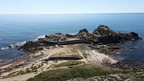 imágenes aéreas de una construcción celta tradicional situada en una pequeña península separada de la tierra por un istmo de arena en la costa de galicia