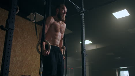 strong bearded male athlete performs push-ups on gym rings in slow motion in the gym