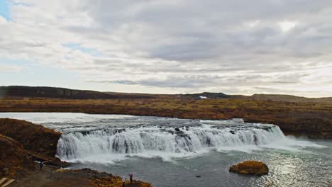 Pan-past-the-beautiful-Faxi-waterfall-in-rural-Iceland-and-slowly-revealing-a-long-river-running-through-a-scenic-landscape