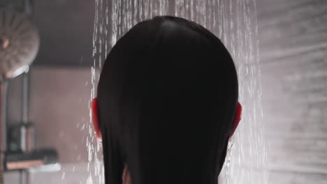 el agua cae en la cabeza fluyendo a lo largo del cabello de la dama. la mujer morena se lava la cabeza en el baño bajo corrientes de agua caliente. procedimientos de spa agradables en casa