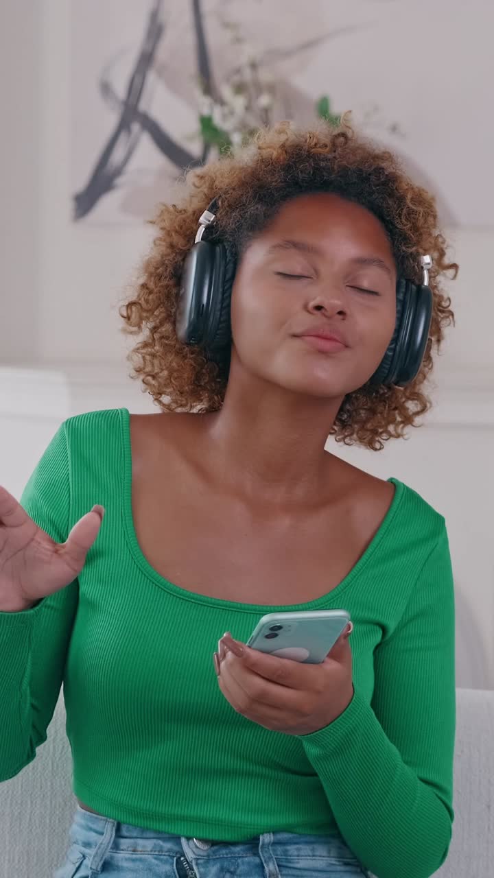 Young african american woman with curly hair wearing headphones listening to