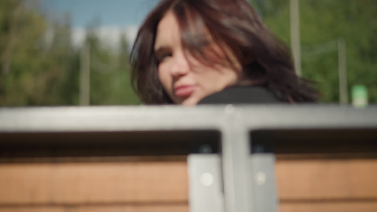 검은 옷을 입은 여성은 빛이 비치는 공원, 울창한 초록색과 멀리 떨어진 나무에서 편안하게 흔들리고, 평온한 야외 휴식을 보이고 공원 환경의 아름다움을 보여줍니다.