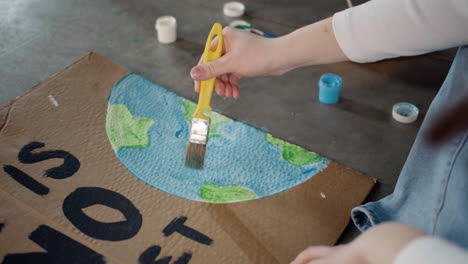 close up of unrecognizable environmental activist painting placards sitting on the floor