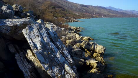 limestone cliffs on shoreline of skadar lake surrounded by mountains, washed by vibrant water on a sunny morning