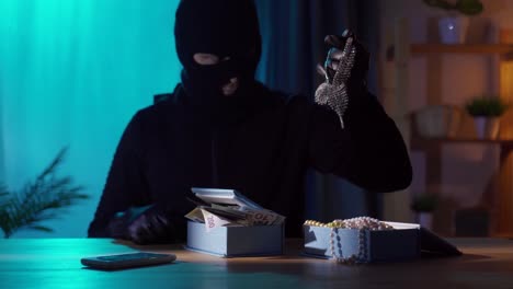 portrait of a robber in a black balaclava with jewelry in his hands