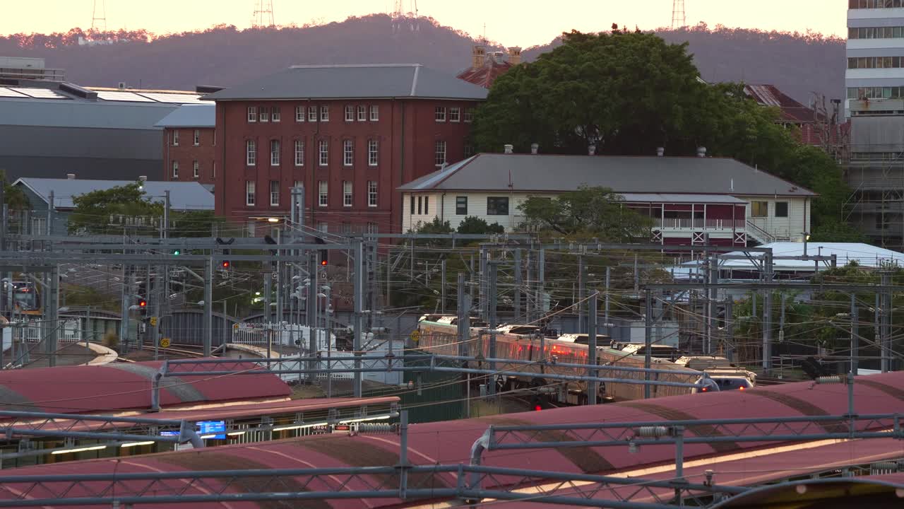 Inbound and outbound trains to Roma Street Station cruise through the station at sunset's golden hour