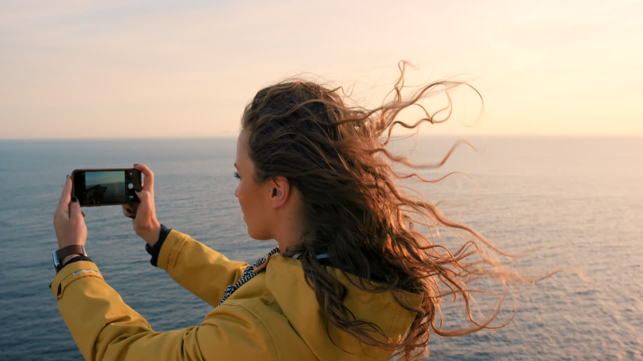 mujer tomando una foto de la puesta de sol sobre el océano